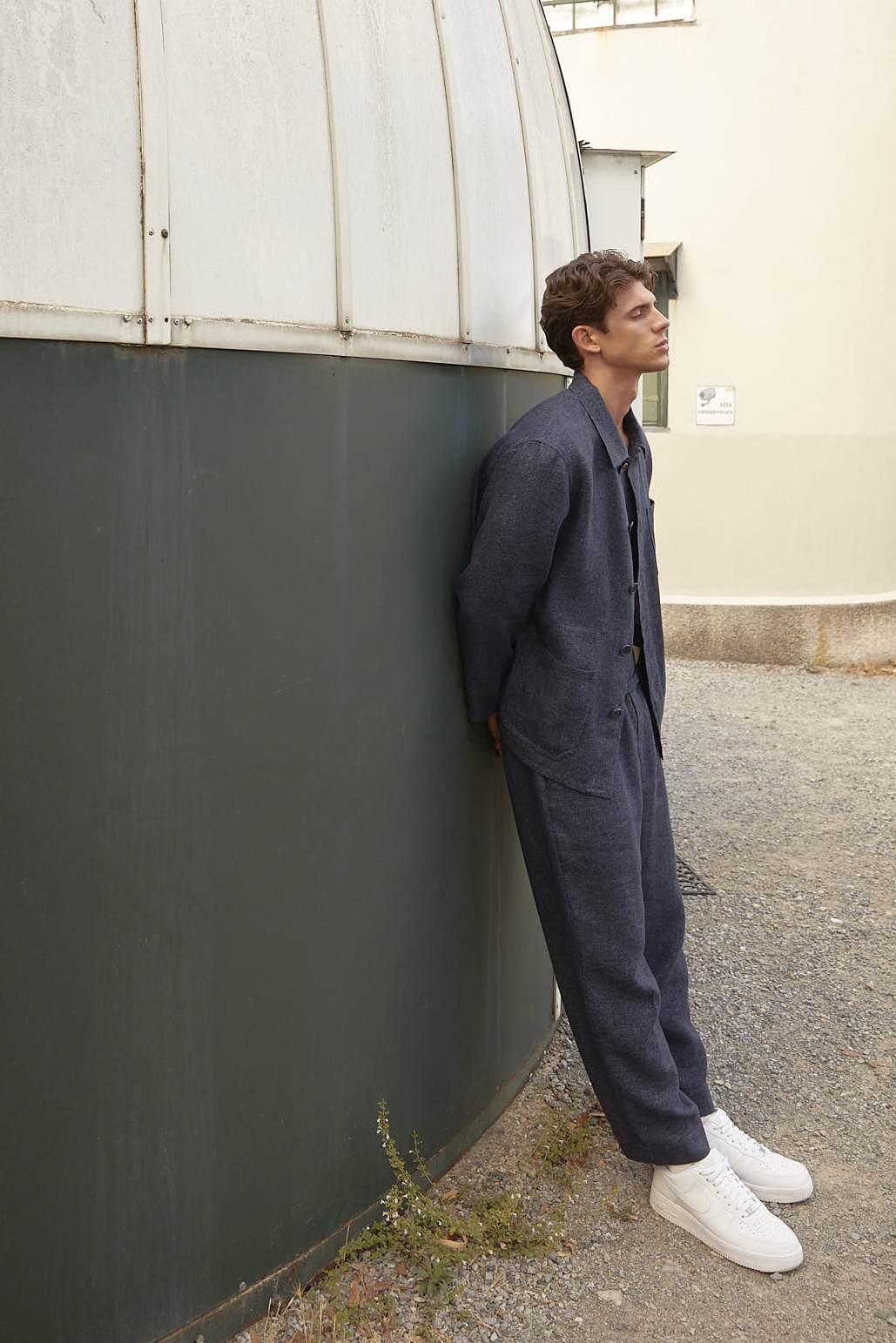 Man in navy blue jumpsuit leaning against green wall in urban setting