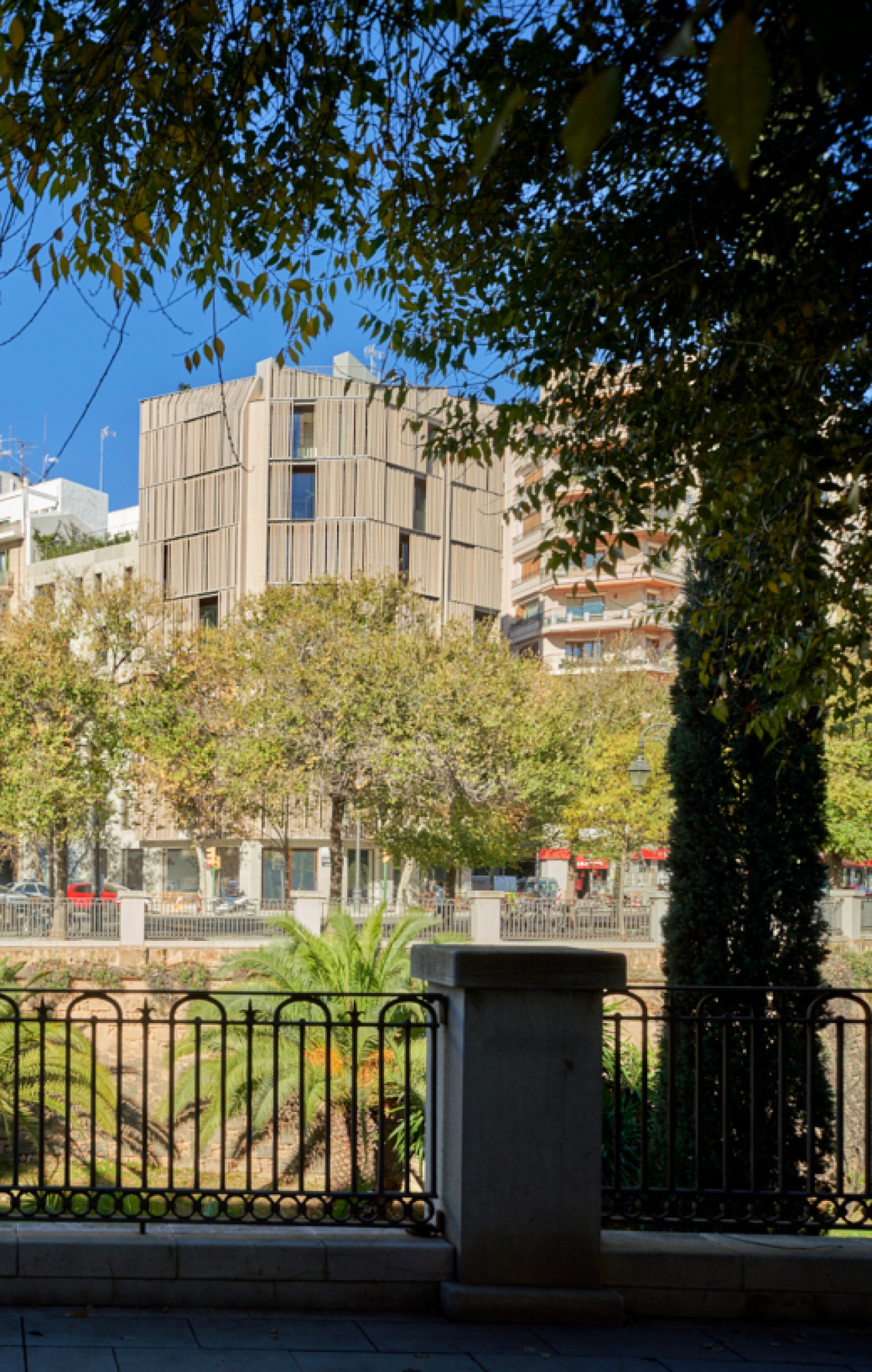 Modern building with vertical timber facade viewed through tree branches and metal railing