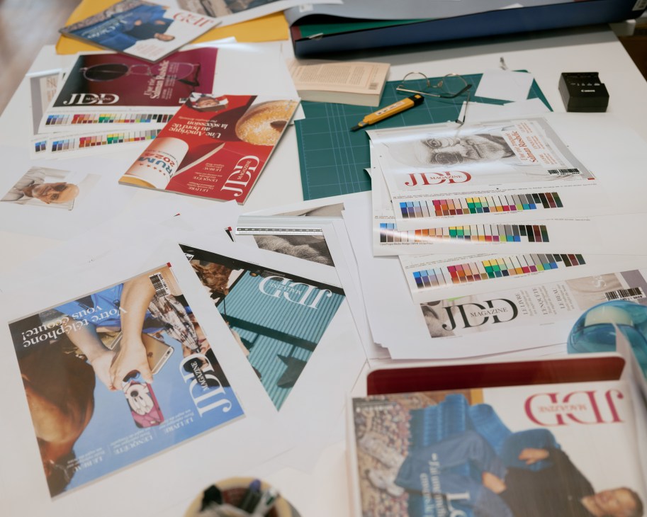 Cover proofs of JDD Magazine spread across a white table with color swatches and design materials
