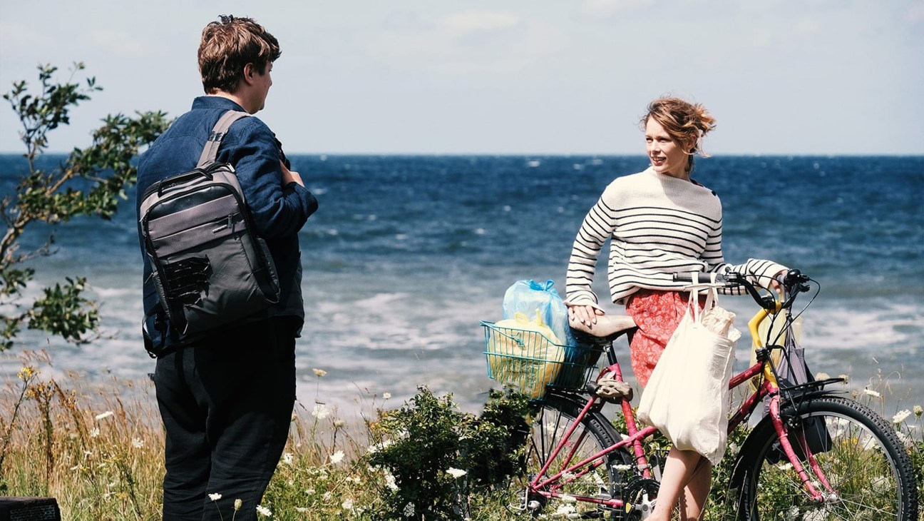 Man with backpack talking to woman with bicycle by seaside coast
