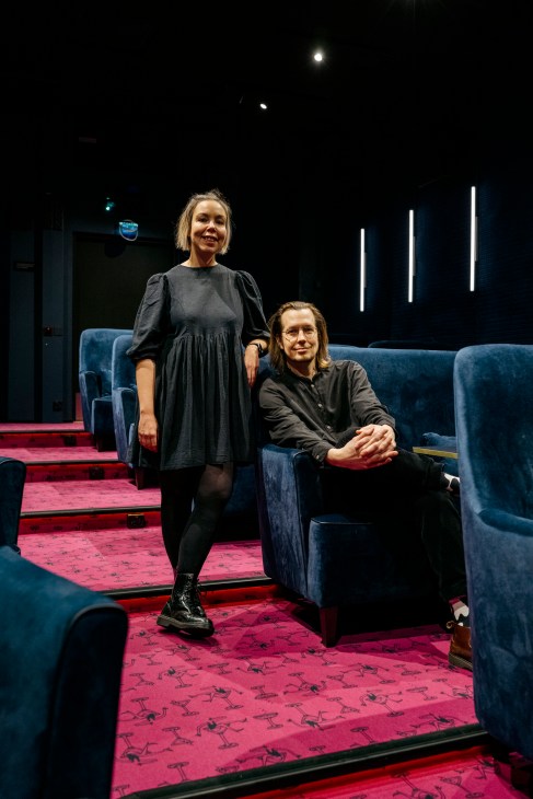 Hanna Hynynen and Atte Laurila standing in cinema with blue velvet seats and red patterned carpet