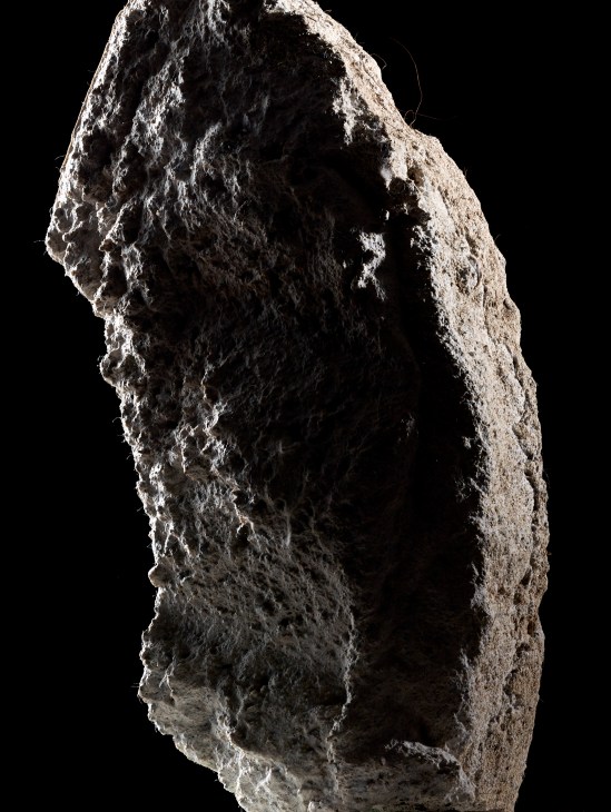 Rough-textured gray concrete or cement material sample with irregular, porous surface against black background