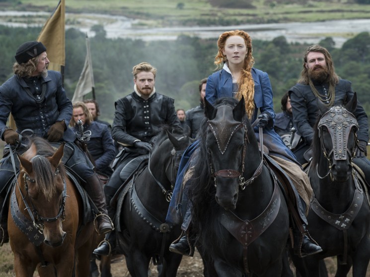 A period drama scene of a red-haired noblewoman on horseback leading a group of riders in dark historical costumes across a misty landscape.
