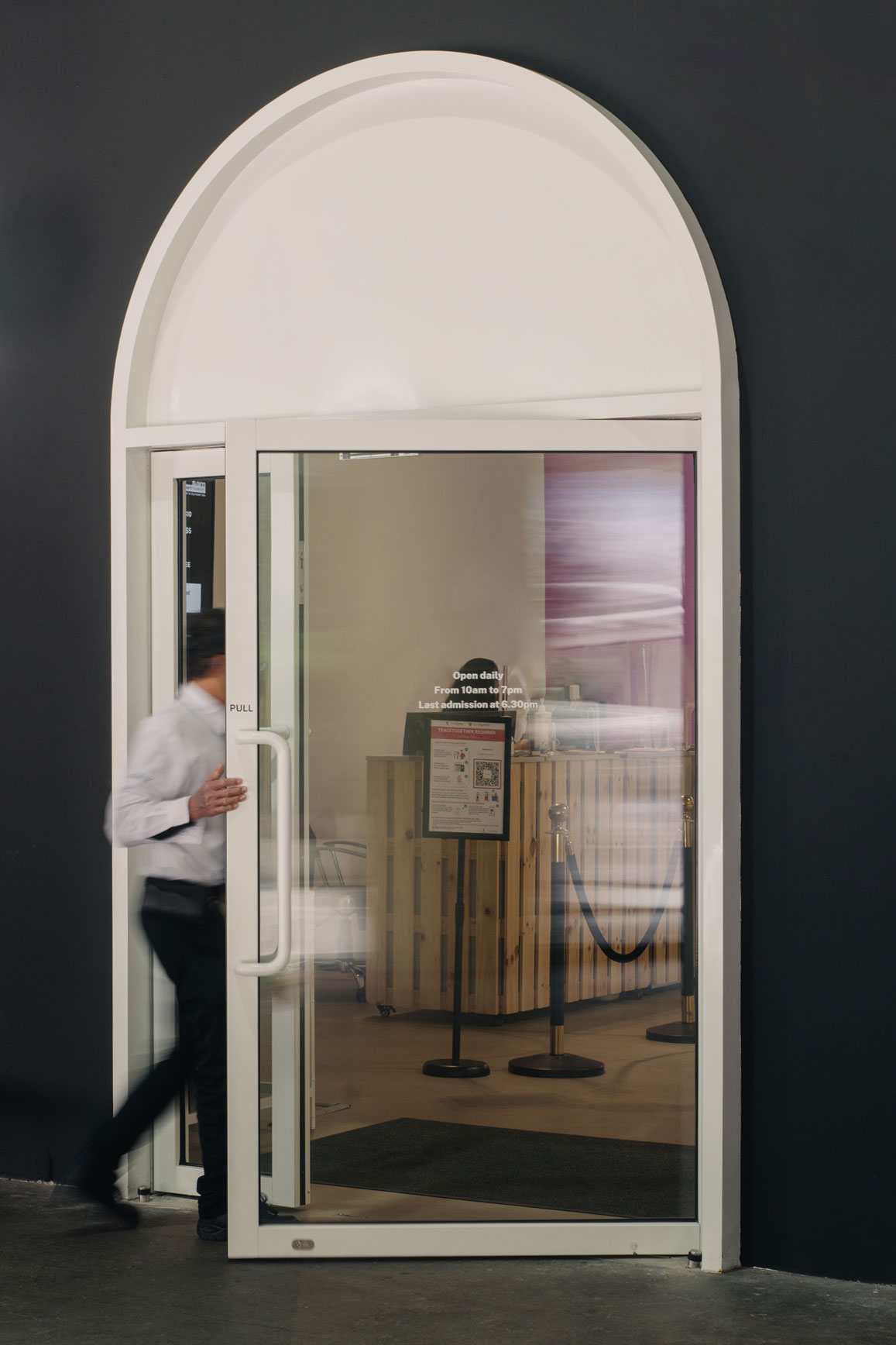 Person in white shirt entering through arched glass doorway of Singapore Art Museum's warehouse space