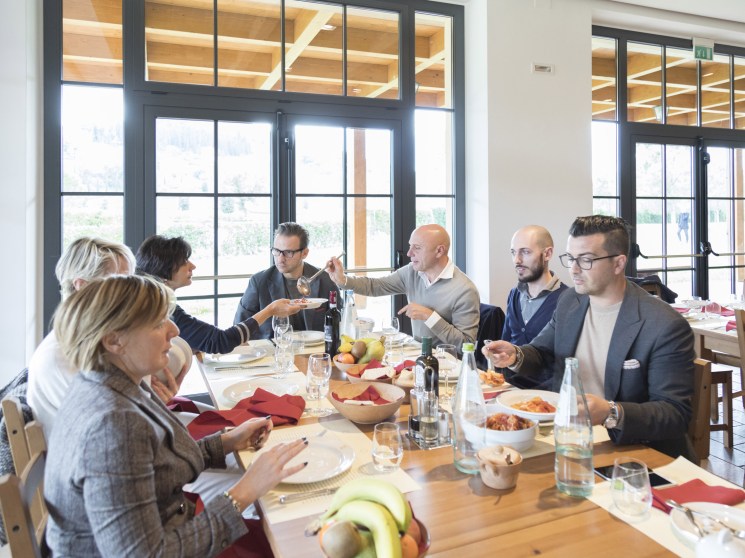 A group of professionals sharing a meal around a long table in a bright, modern dining room.