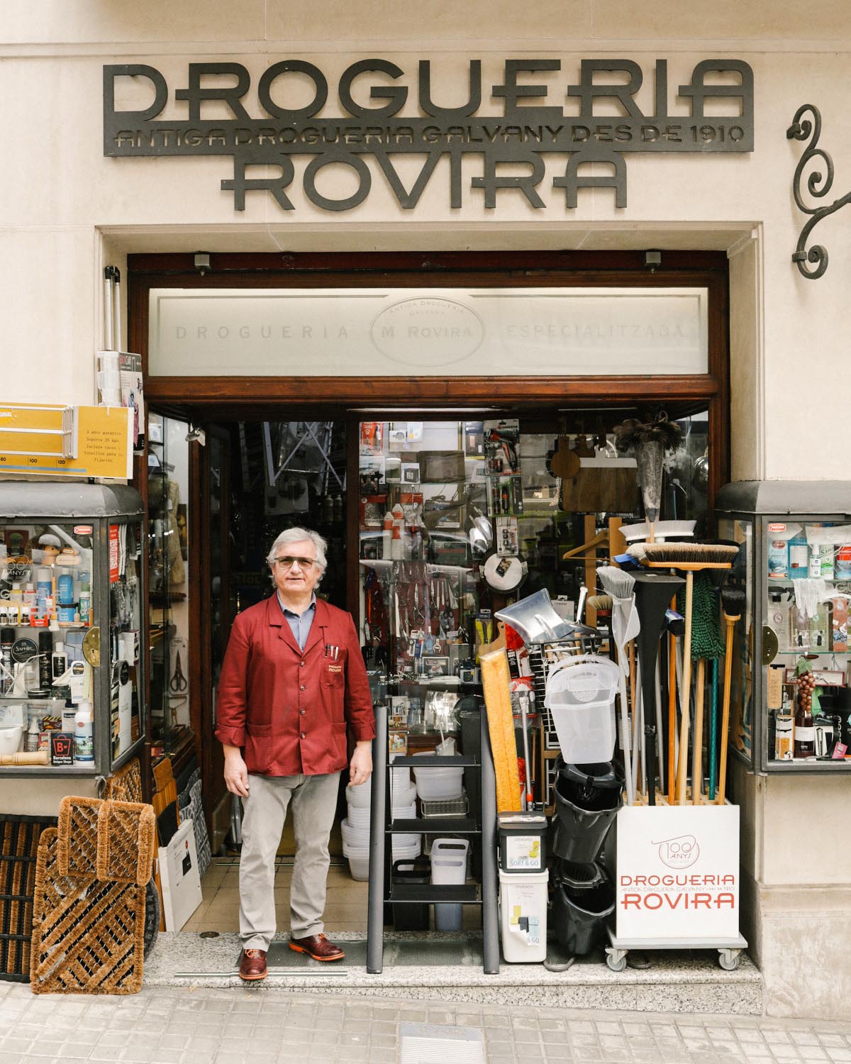 Man in red cardigan standing in doorway of hardware store filled with organized shelves of household items