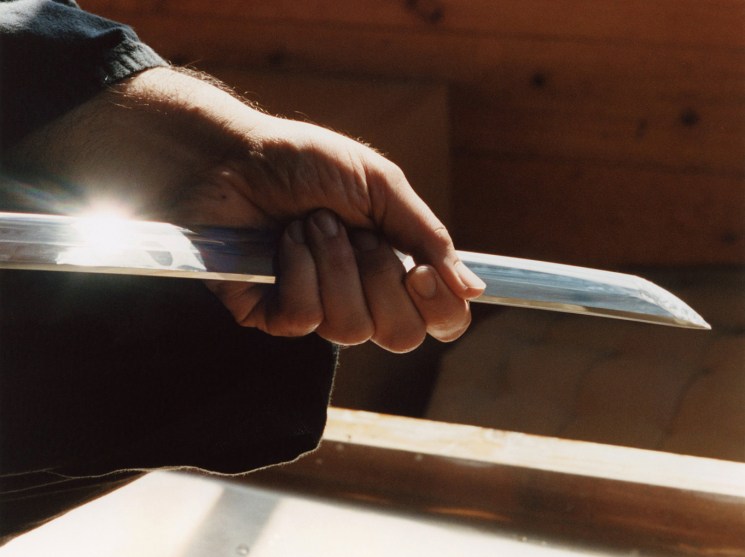 Sotaro Matsumura working with precision at his whetstone, wearing traditional indigo samue robes in his cedar workshop
