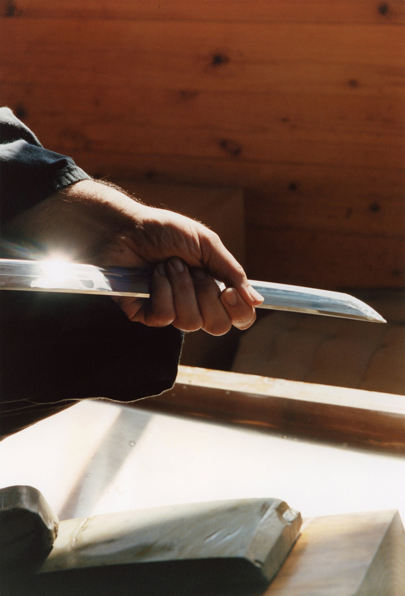 Sotaro Matsumura working with precision at his whetstone, wearing traditional indigo samue robes in his cedar workshop