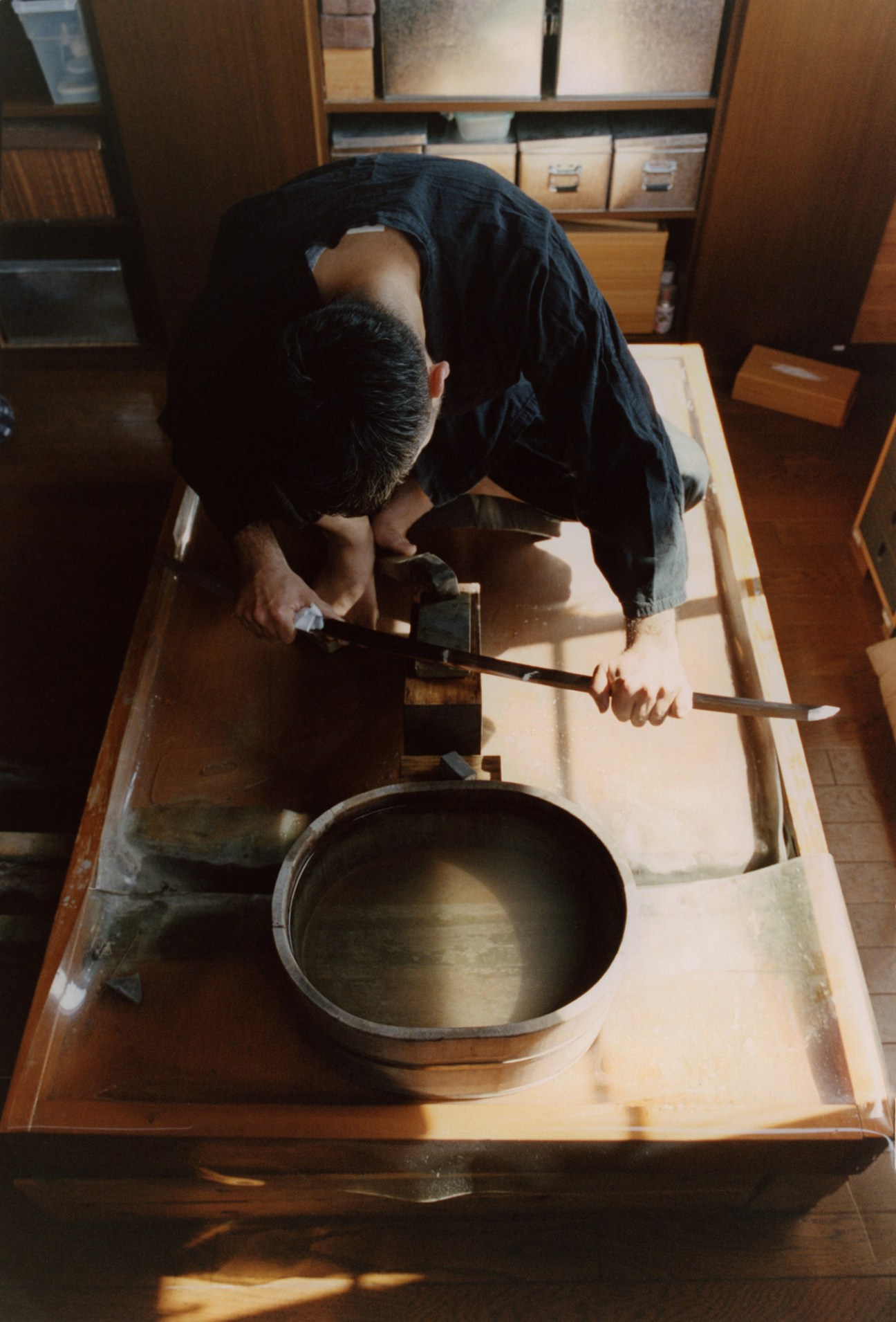 Matsumura carefully examining a sword blade mid-polish, checking the metal's surface for imperfections