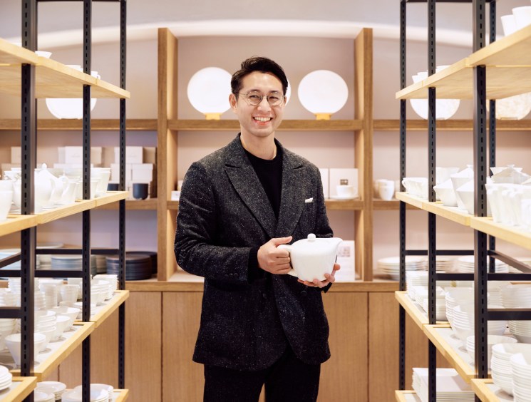 Naoki Mitani standing in porcelain showroom holding white bone china teapot surrounded by shelves of white tableware