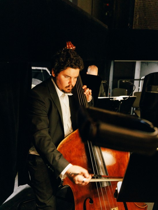 Male double bass player in formal concert attire performing during rehearsal at Deutsche Oper