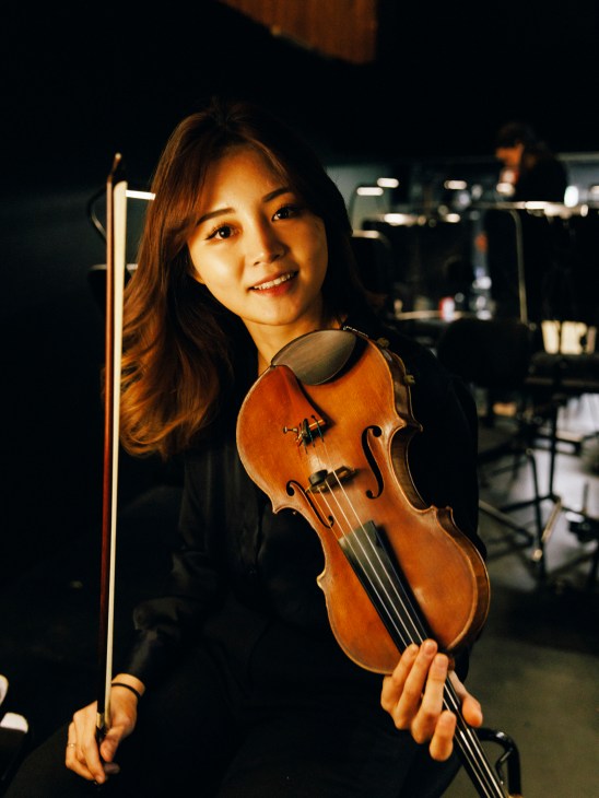 Young woman violinist holding violin and bow in orchestra rehearsal space