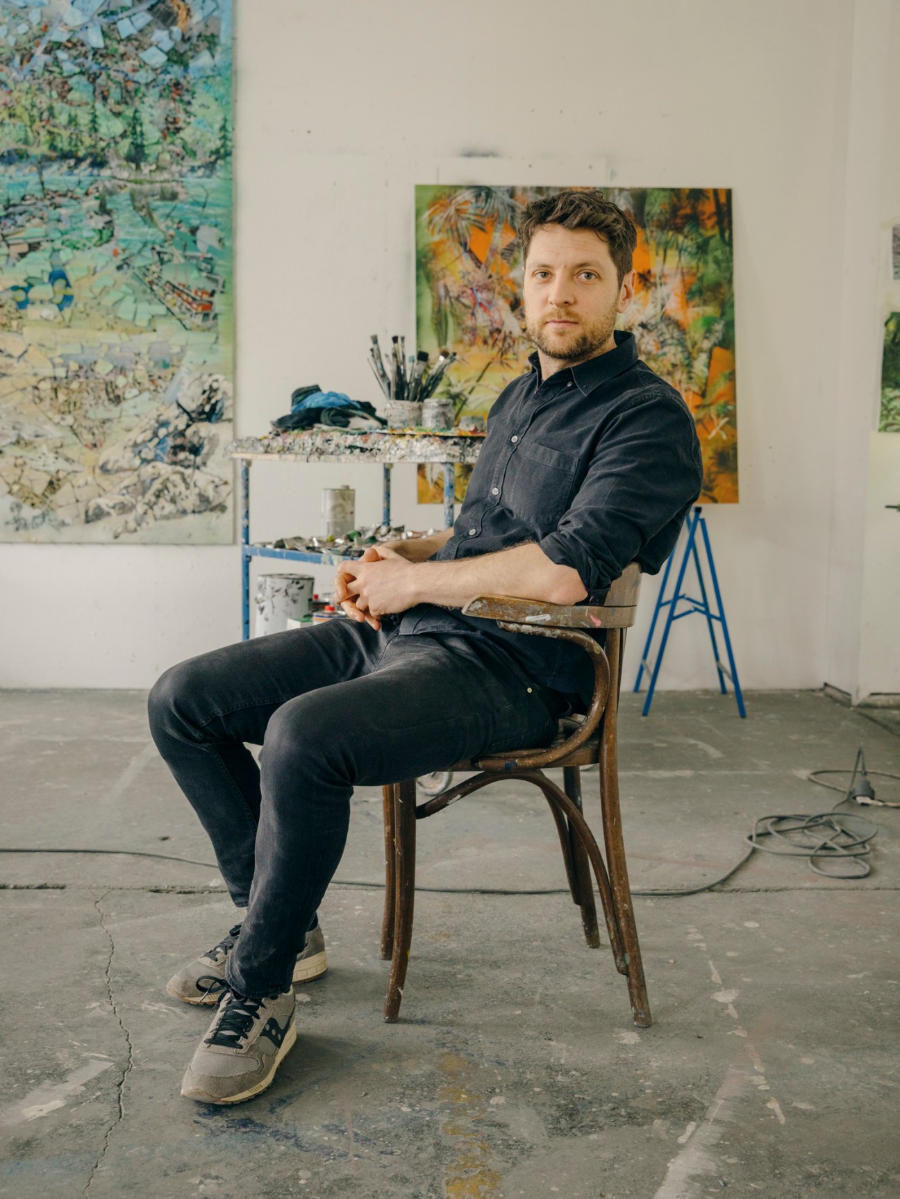 Philipp Fürhofer sitting in a chair in his Berlin studio surrounded by artwork and paintings