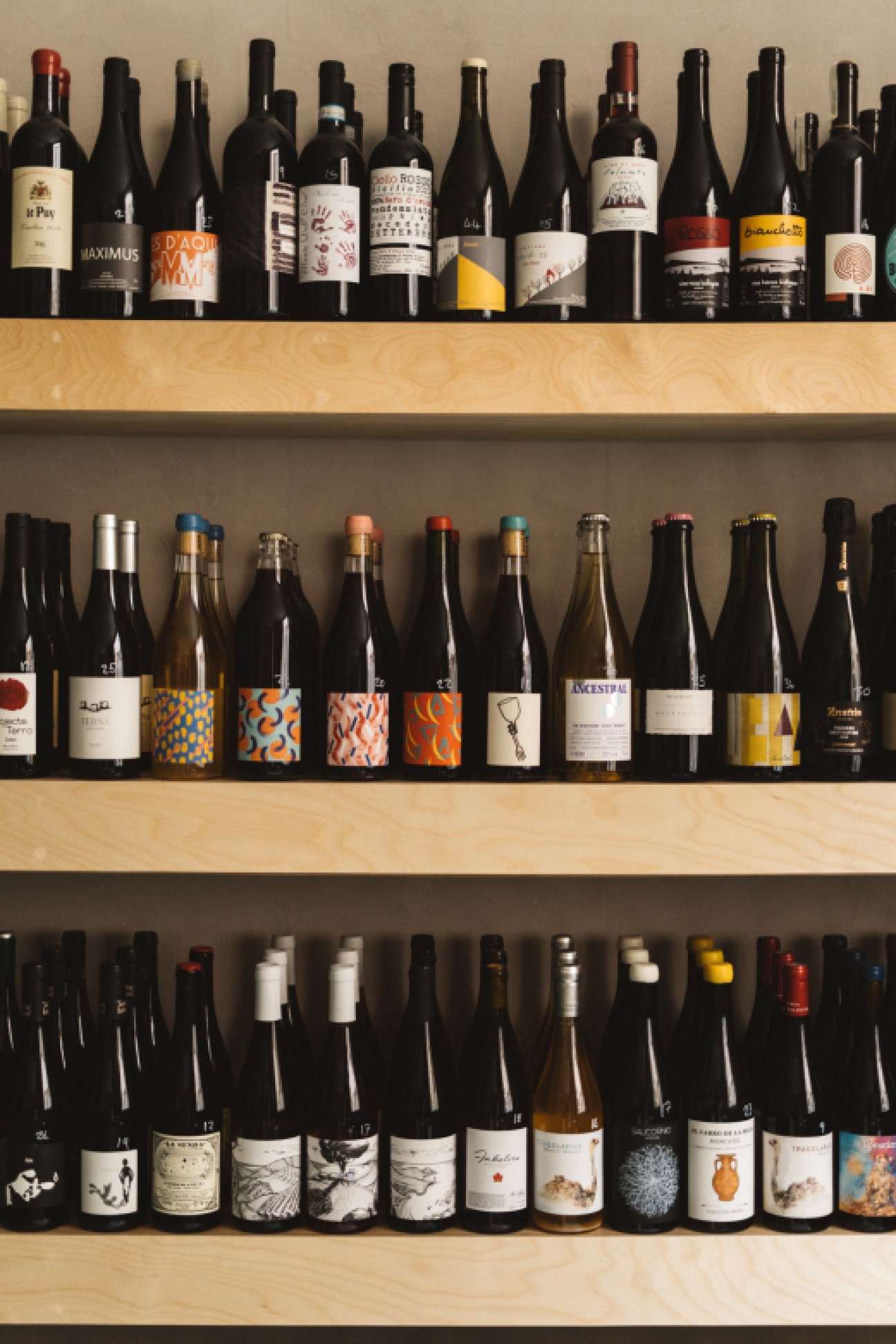 Three shelves displaying rows of wine bottles with colorful labels and various closure types