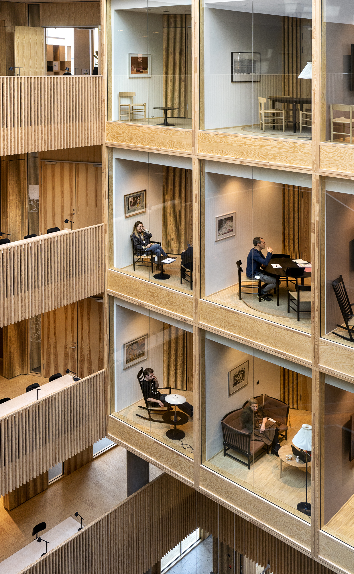 Modern office interior with multi-level glass-walled workspaces featuring wood panels and residential-style furnishing
