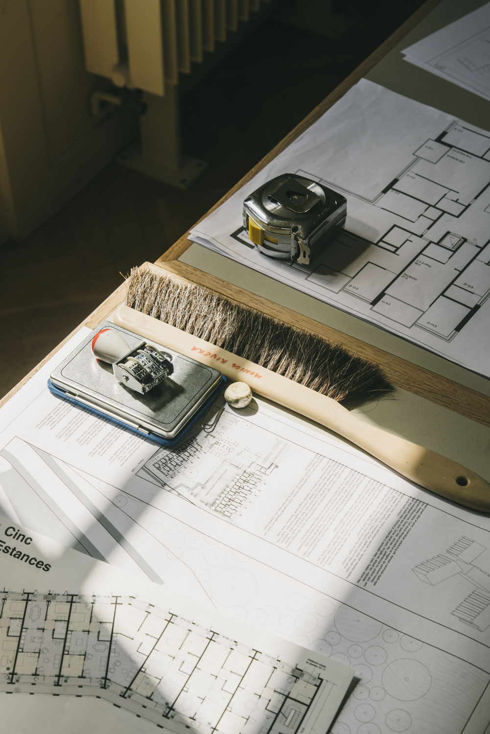 Architectural plans and design tools on a wooden desk with a brush and measuring instruments.