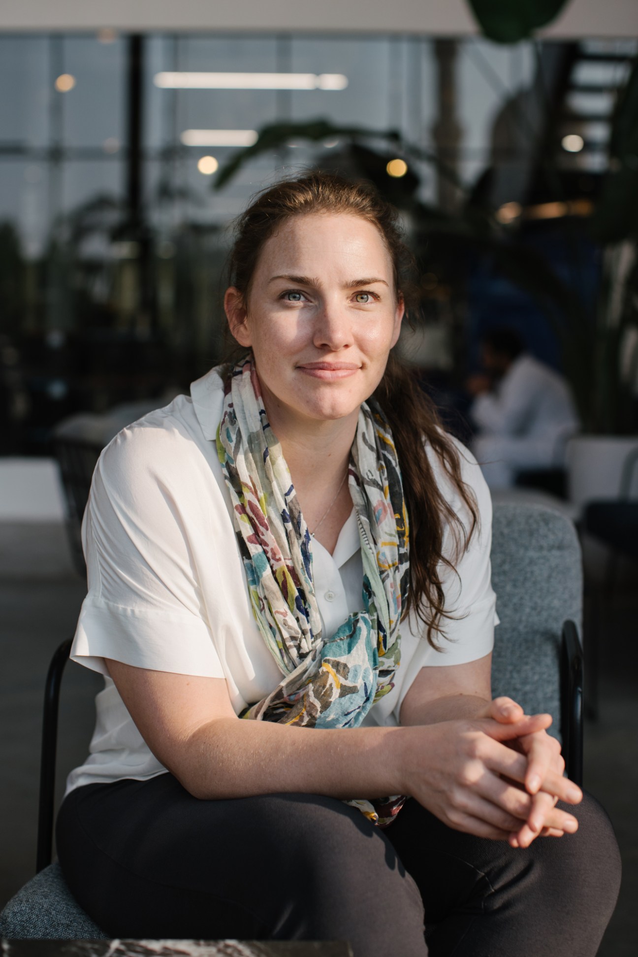 Woman sitting in modern office kitchen wearing white shirt and patterned scarf