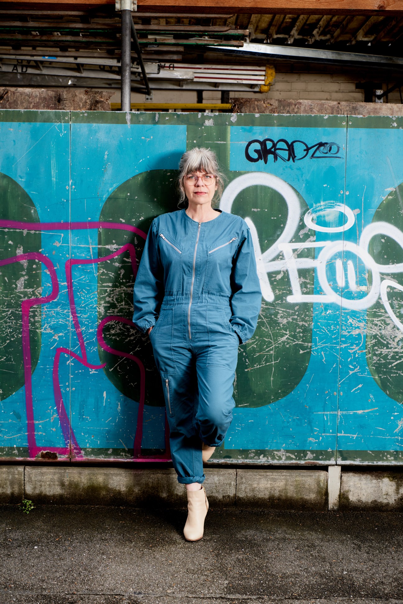 Woman in blue denim jumpsuit standing against colorful graffitied wall in urban setting