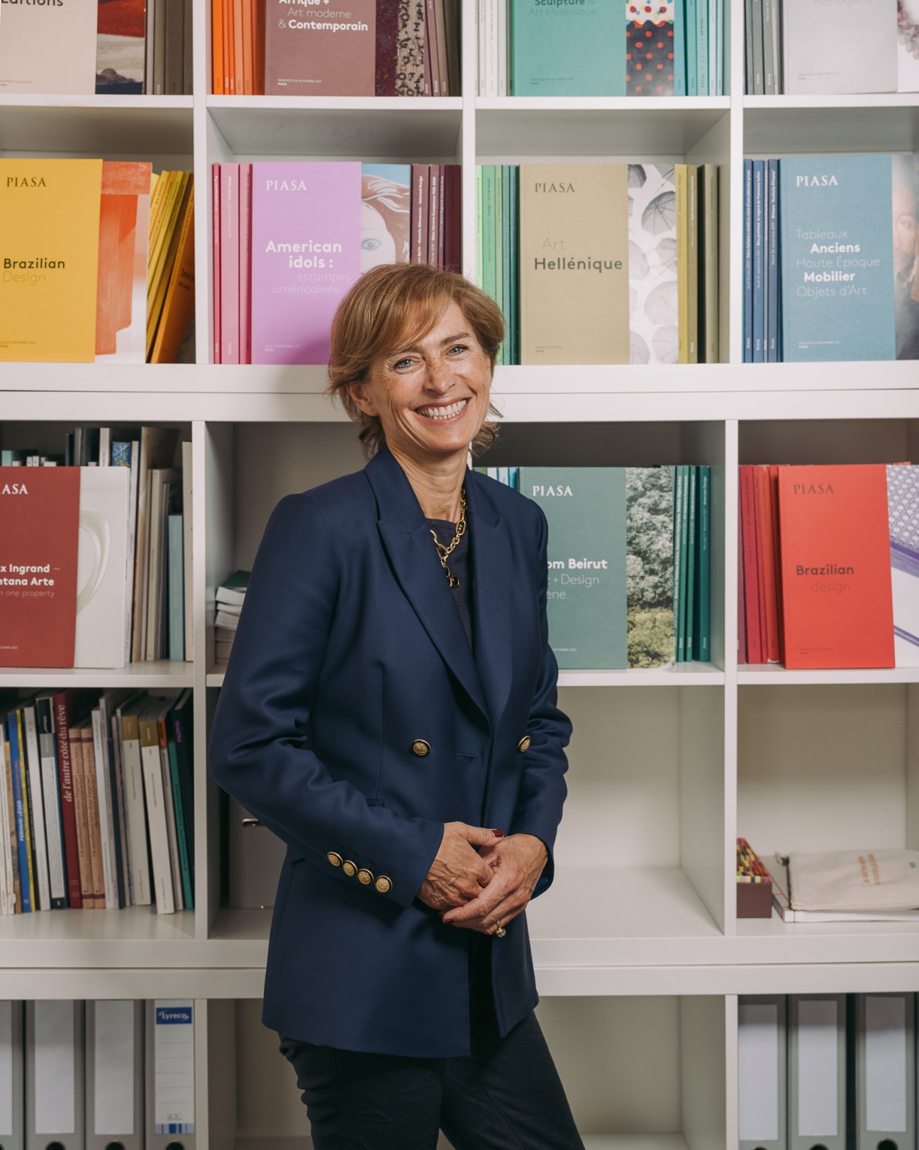 Marie Filippi stands smiling in front of white bookshelves filled with colorful art books