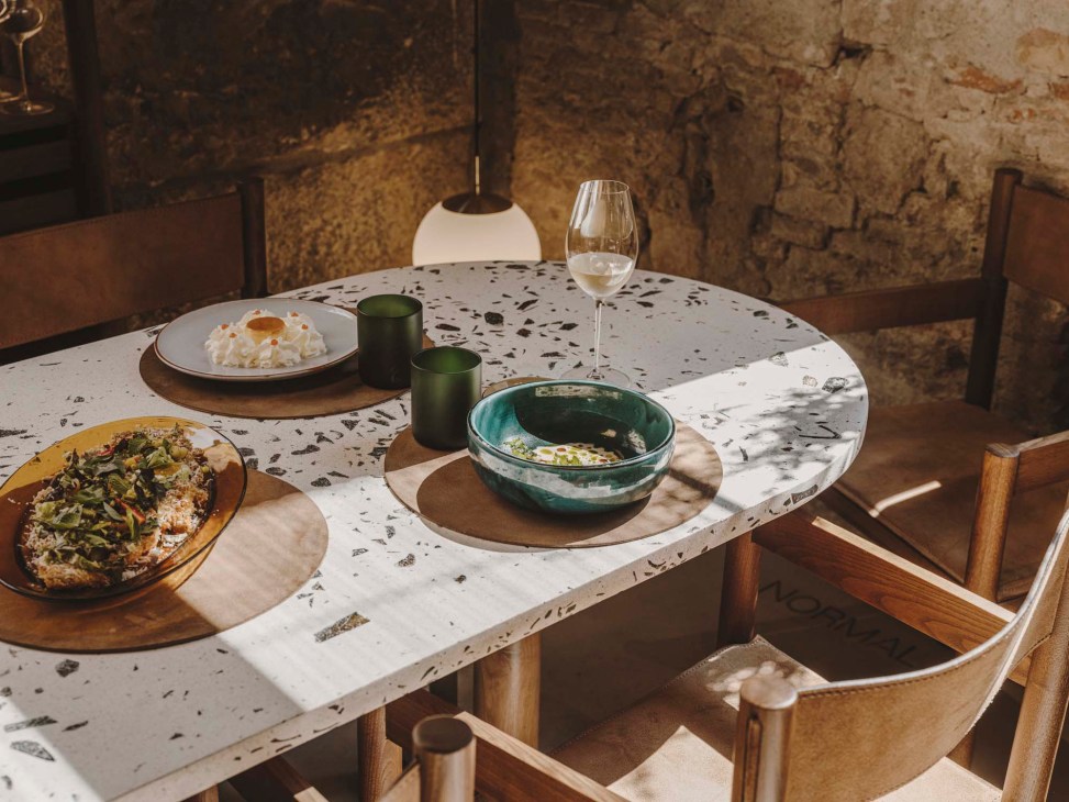 Elegant table setting with terrazzo surface displaying artfully plated dishes, wine glass, and ceramic bowls in rustic interior