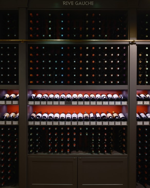 Wine bottles displayed in a modern cellar storage system with organized rows and 'RIVE GAUCHE' sign above