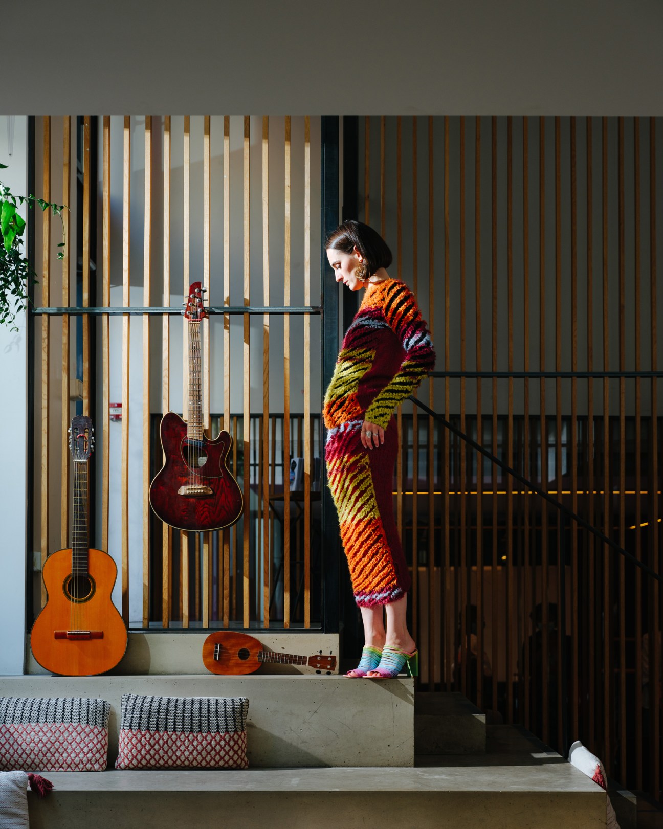 Julie Budet of Yelle wearing a colorful striped knit dress standing on stairs in a modern interior