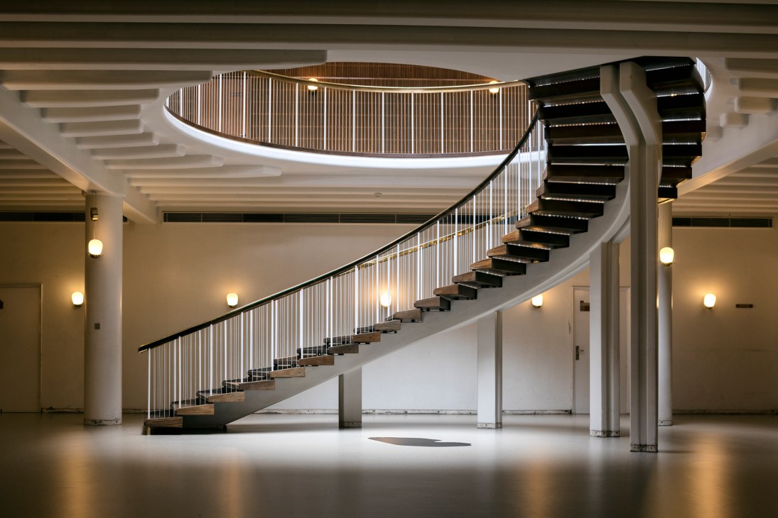 Modern curved staircase with vertical cable railings and warm lighting in Aarhus City Hall interior