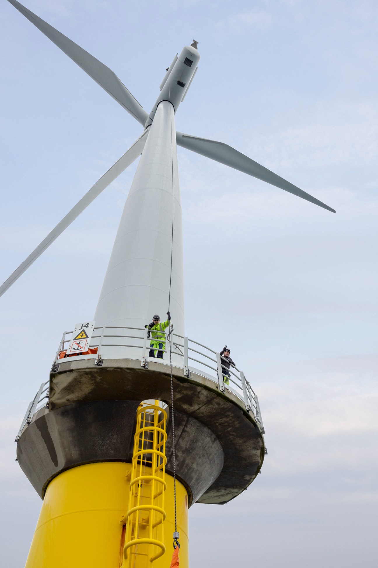 Maintenance workers in high-visibility jackets standing on platform of offshore wind turbine