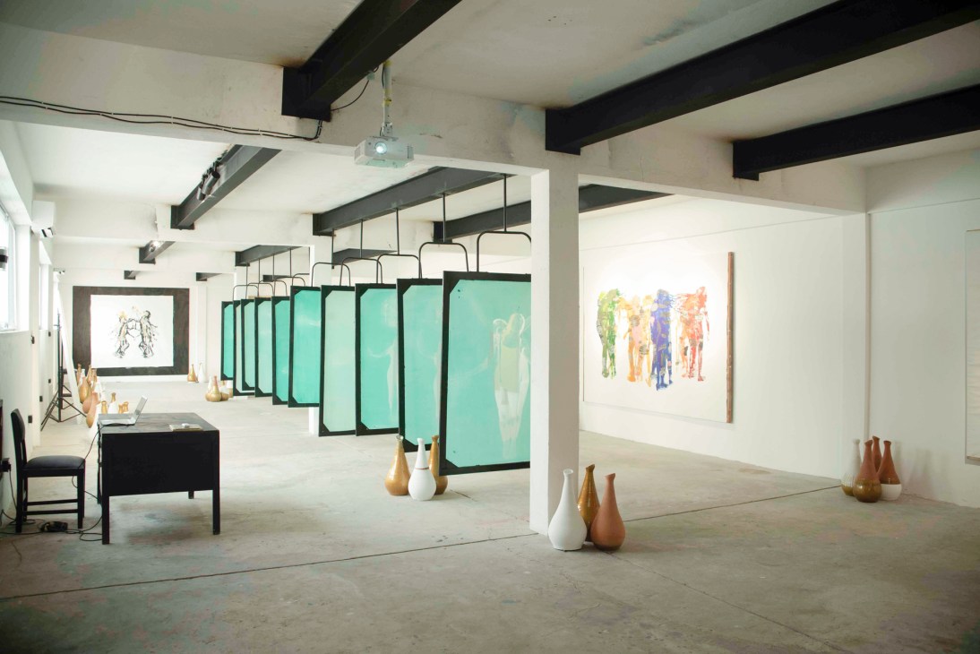 Modern gallery interior with concrete floors, exposed beams, hanging turquoise panels, and colorful artwork on white walls