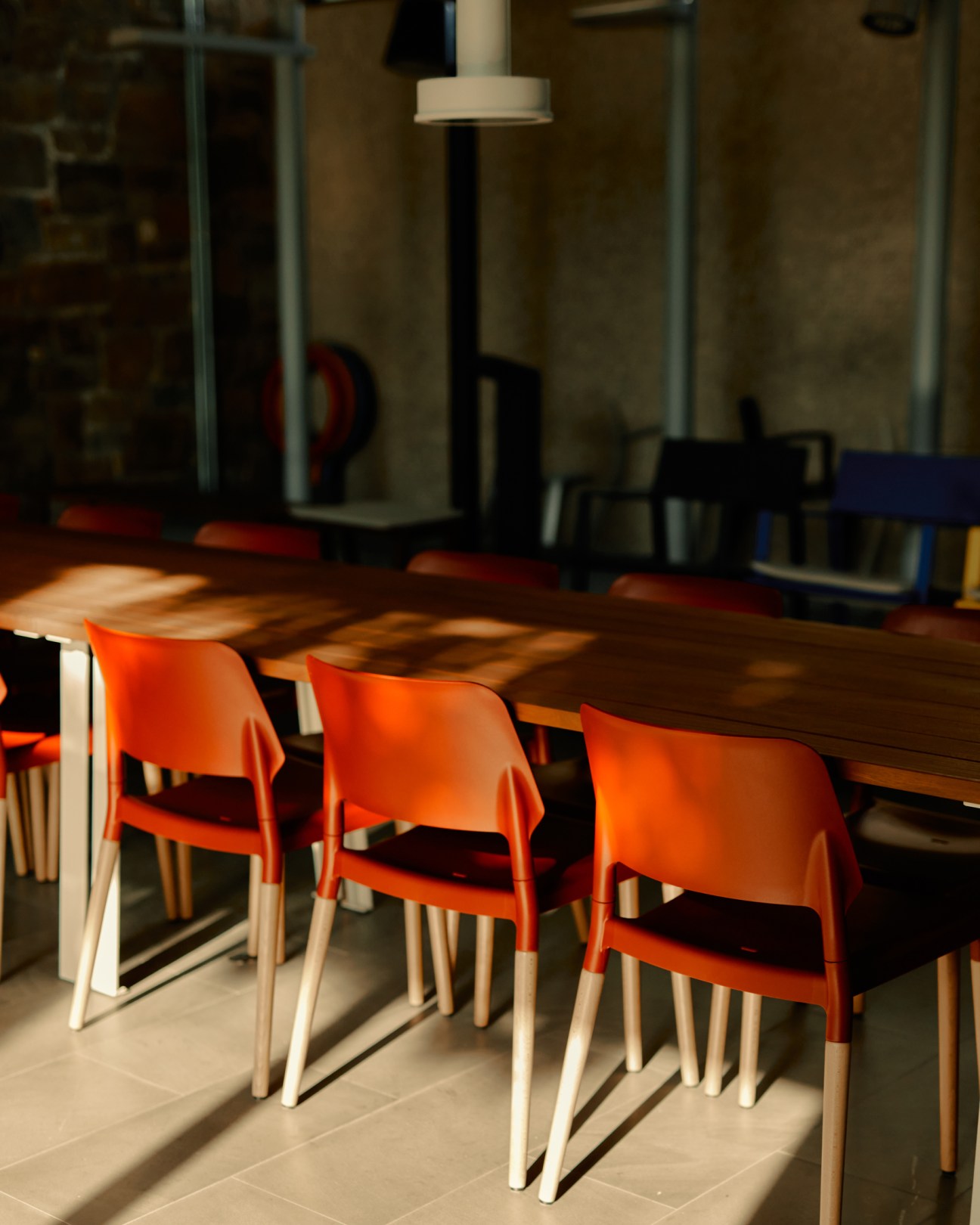 Three art dealers seated at a wooden table with orange chairs in a modern gallery space.