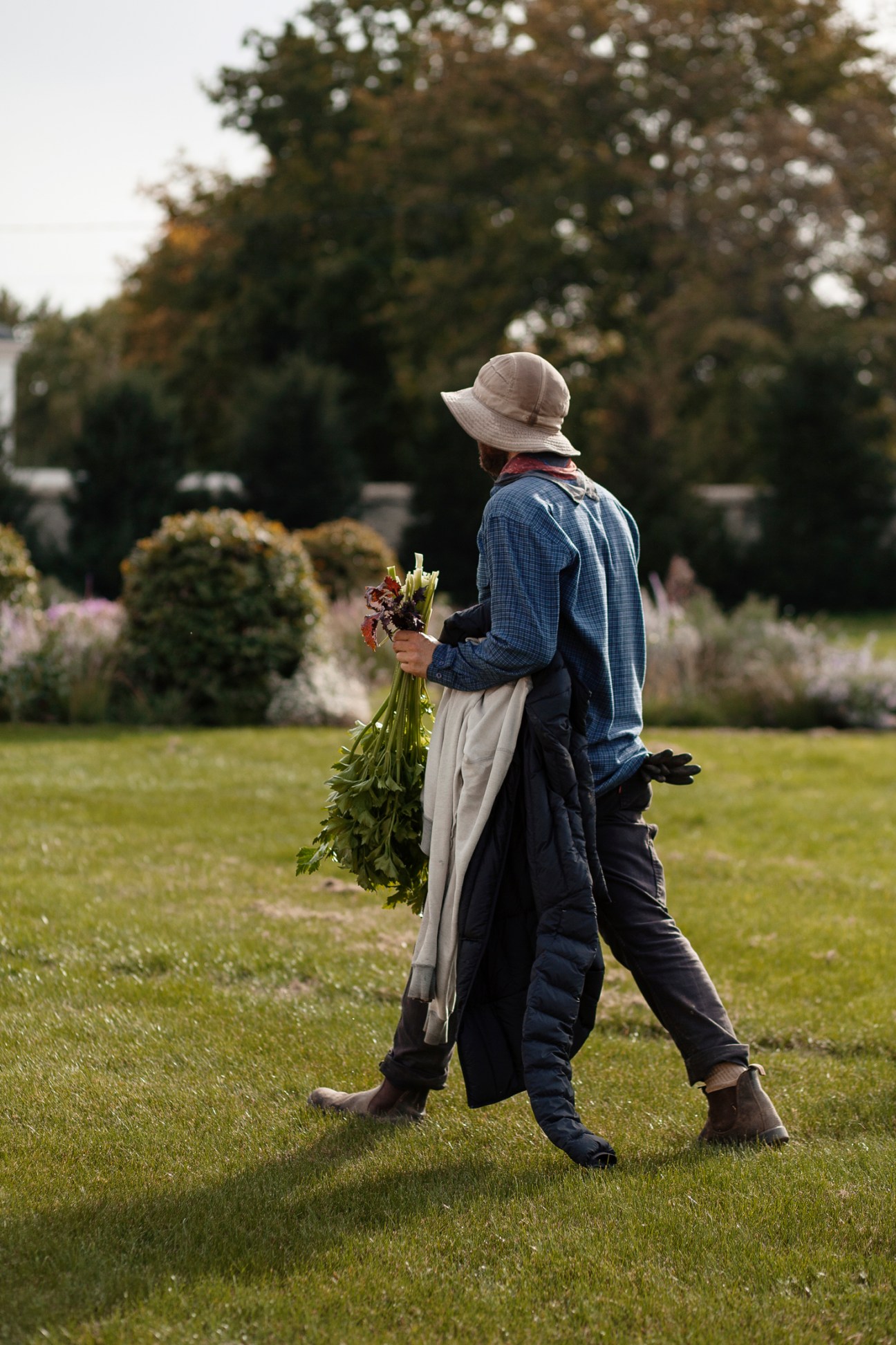 Man in traditional Bavarian lederhosen and blue shirt holding flowers in a garden.