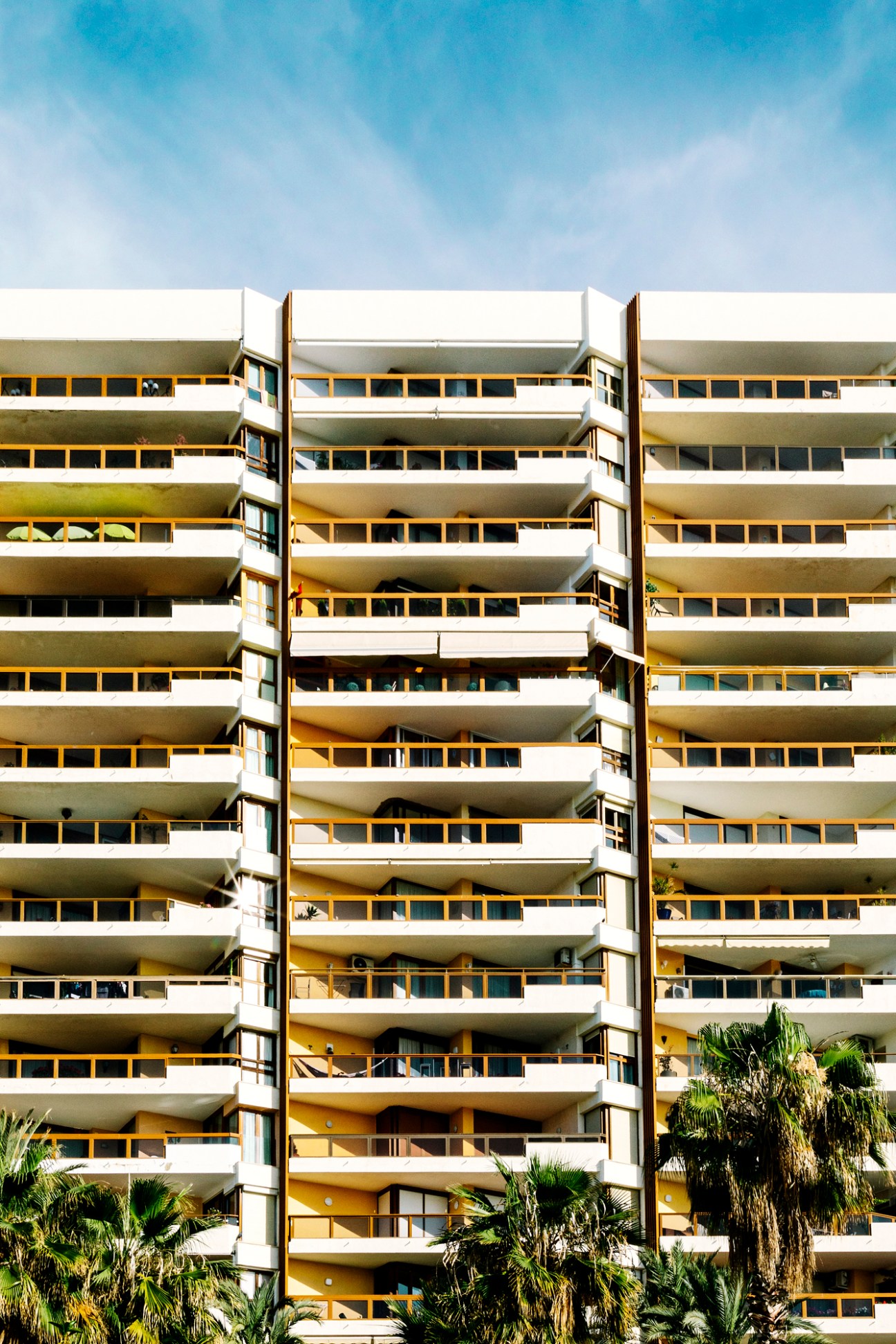 Modernist apartment building Melilla 31 with stacked curved balconies, white railings, and golden-yellow window frames against blue sky.