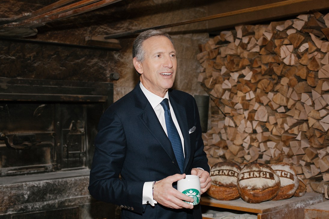 Howard Schultz, CEO of Starbucks, holding a coffee cup in front of stacked firewood.