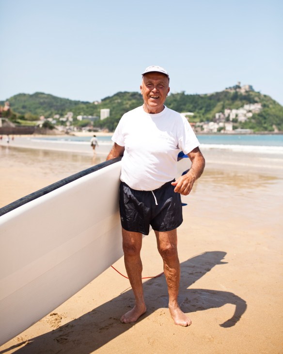 Elderly man in white cap and t-shirt standing beside white boat on Playa de la Concha beach in San Sebastián