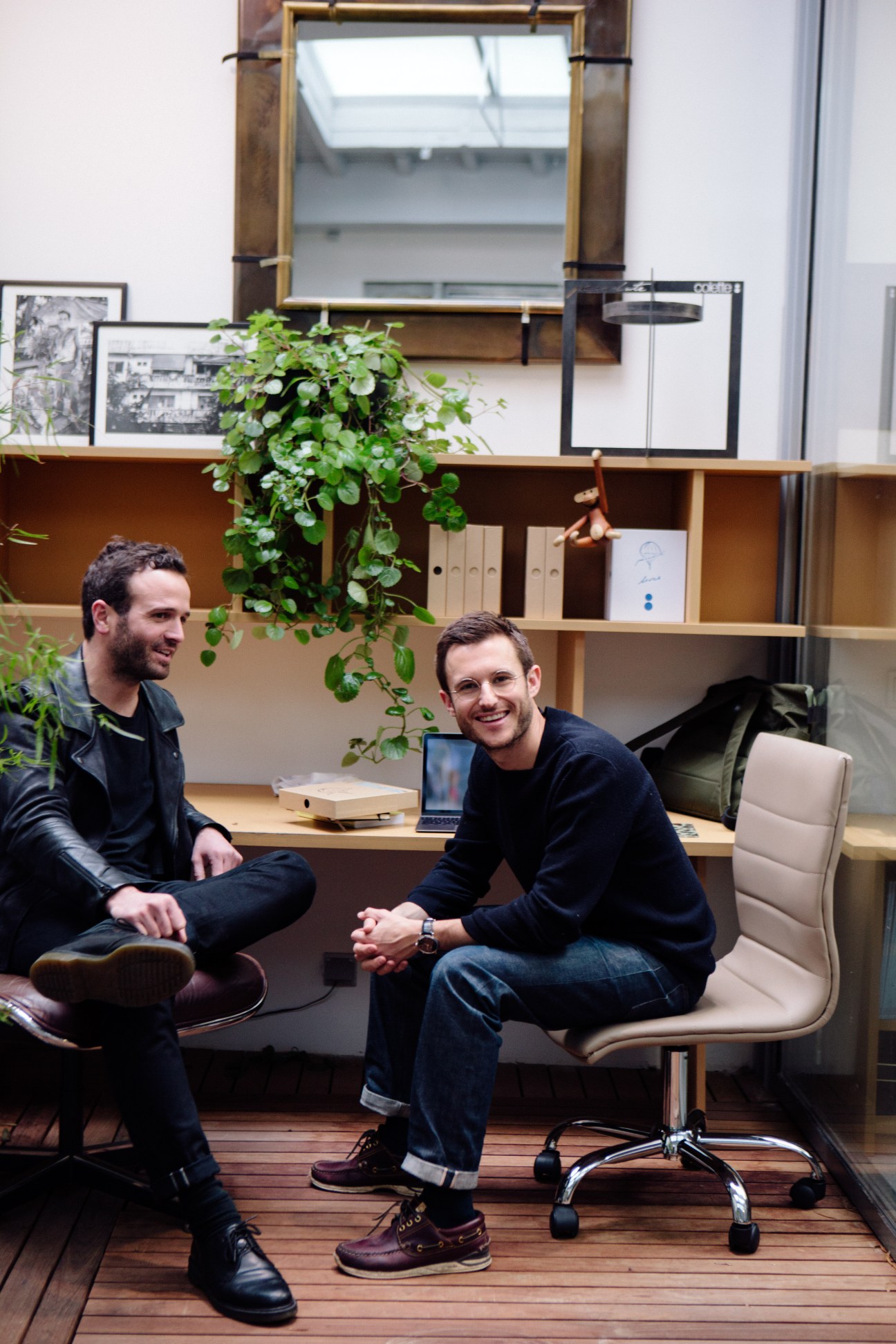 Two men sitting in a modern office with wooden shelving and plants