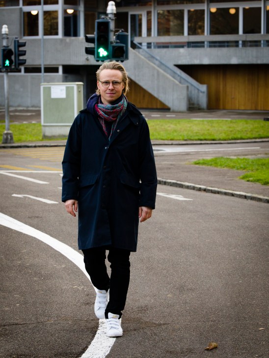 Portrait of Swiss architect Lukas Raeber standing on a street wearing glasses and a dark coat