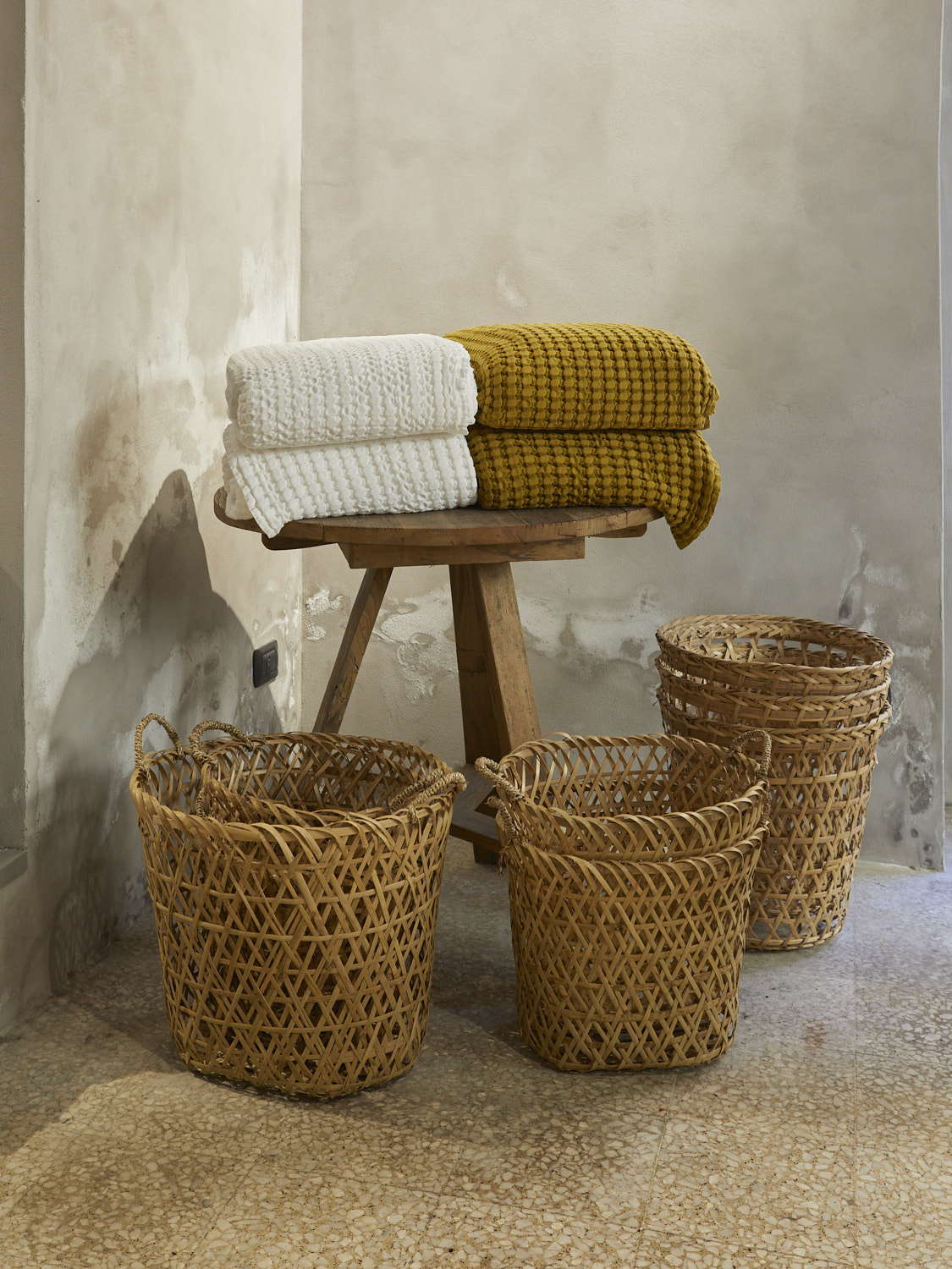 Folded towels and woven baskets displayed on wooden stool against weathered wall