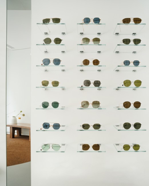 Wall display of various sunglasses mounted on glass shelves in Ahlem's minimalist Paris store
