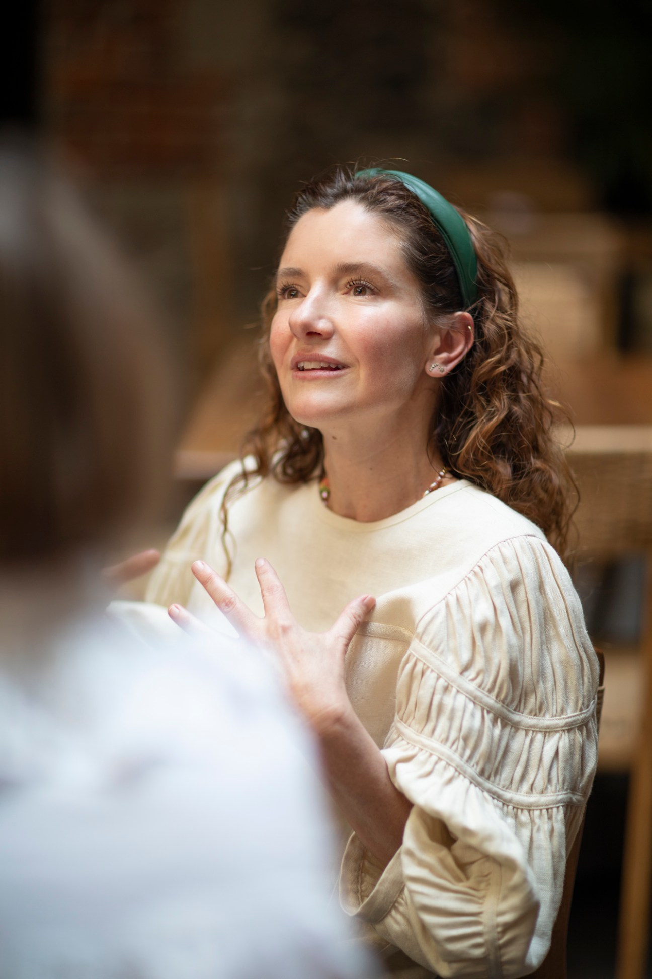 Woman with green headband gesturing expressively while speaking during culinary discussion