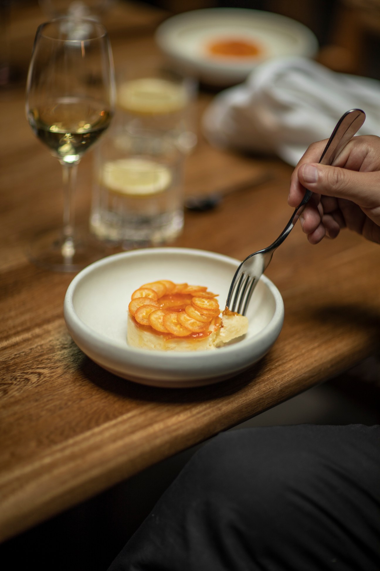 Hand holding a fork cutting into a small tart topped with sliced fruit on a white plate
