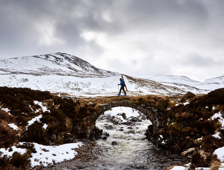 Jamie Kunka skiing across snowy terrain on a stone bridge in Scotland's Cairngorms mountains