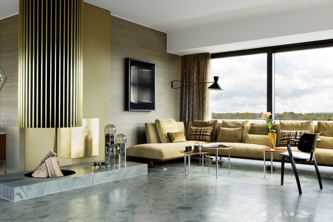 Modern apartment living room with beige sofa, fireplace, and river views through expansive windows.