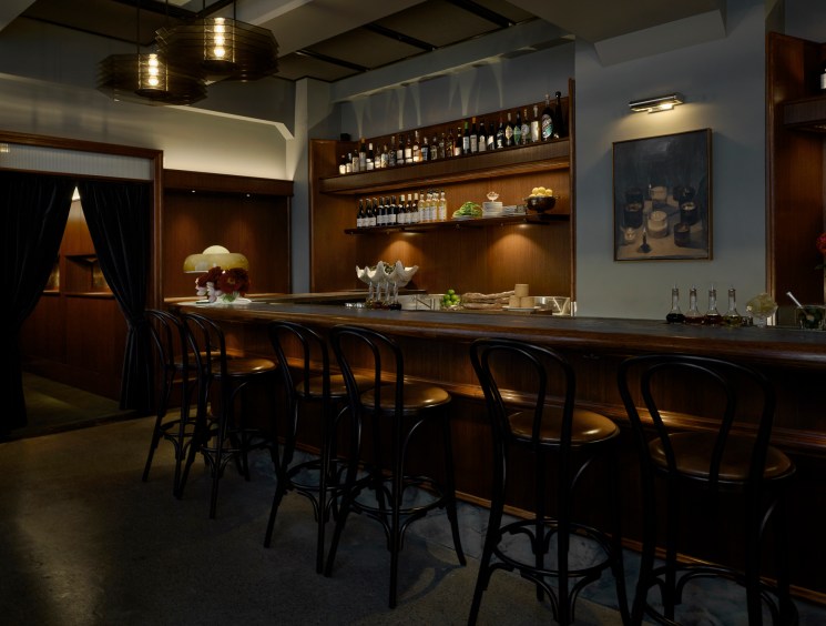 Elegant bar interior with wooden counter, black bar stools, and bottles displayed on shelves behind