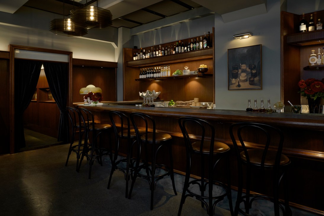 Elegant bar interior with wooden counter, black bar stools, and bottles displayed on shelves behind