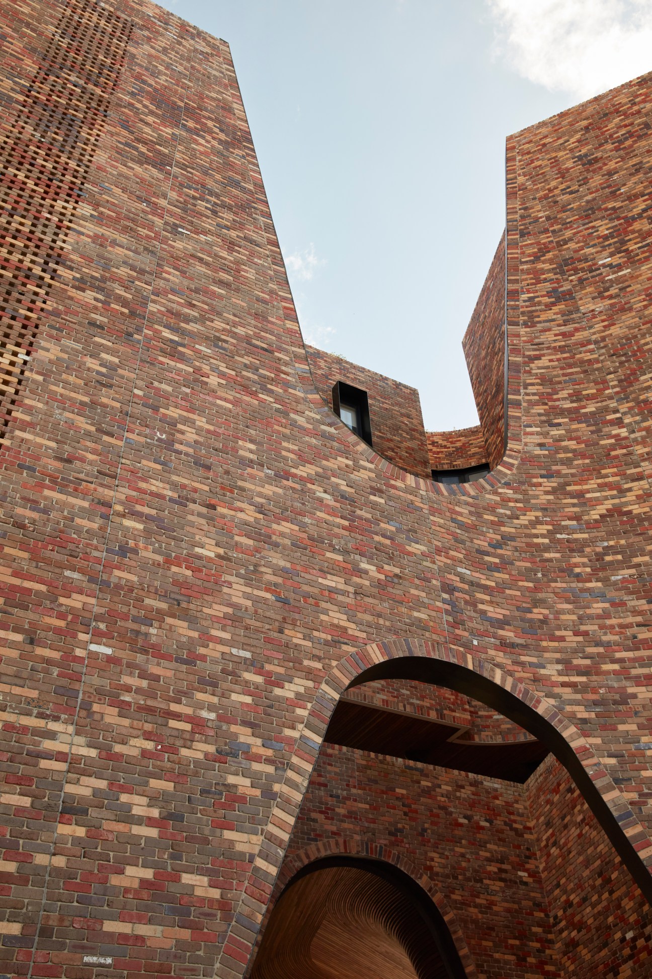 Looking up at curved brick walls with archway openings against cloudy sky