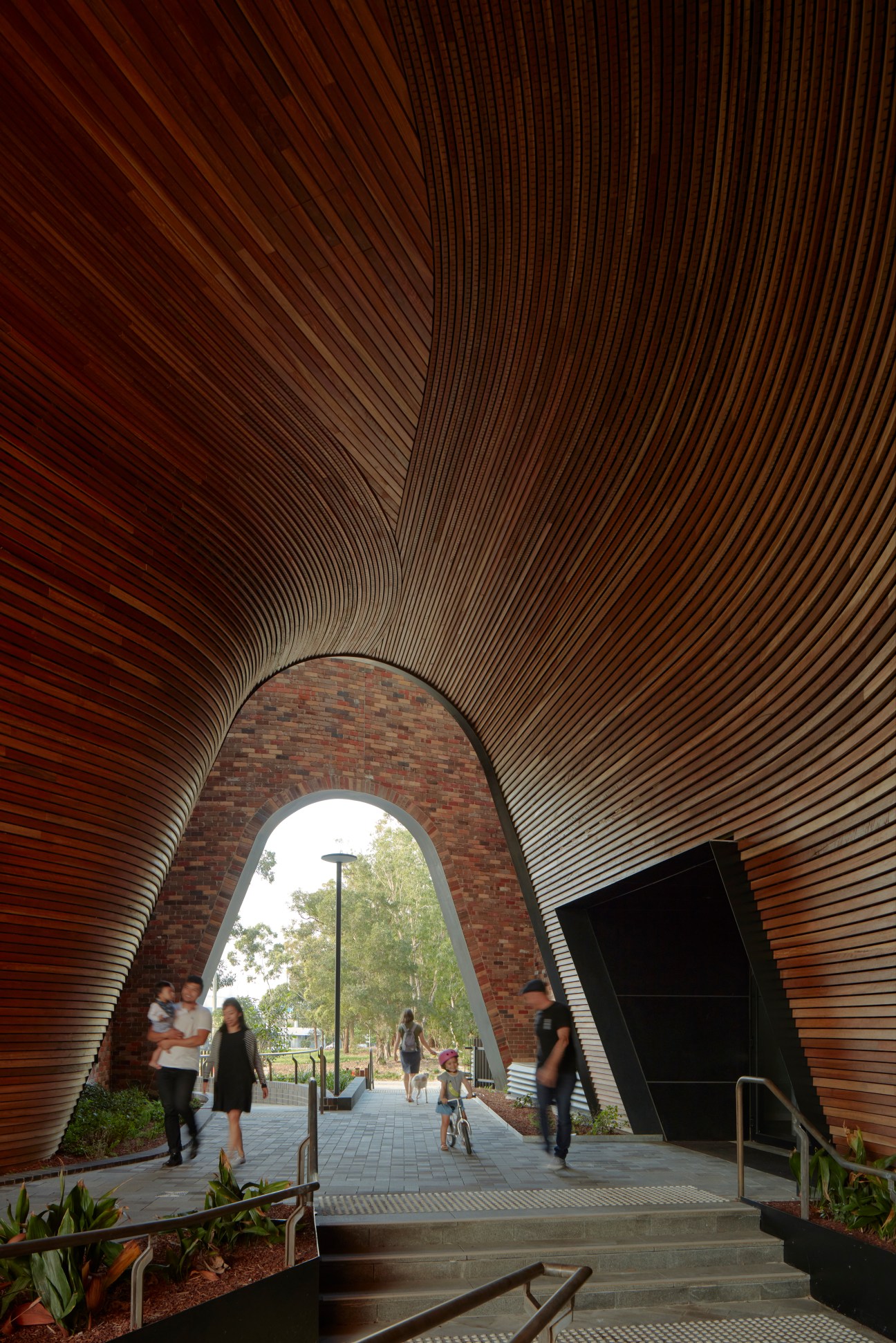 Modern timber-lined archway entrance with brick wall and people walking through at Arkadia apartments Sydney