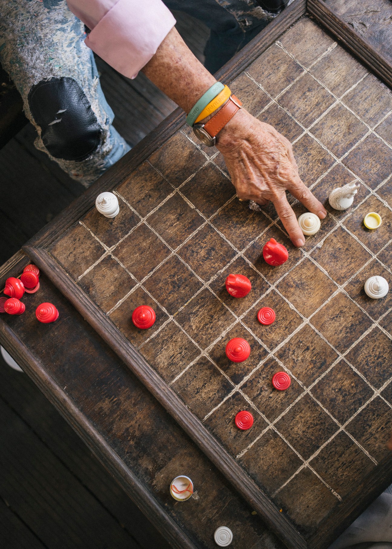A person's hand moves a piece on a wooden chess board with red and white pieces.