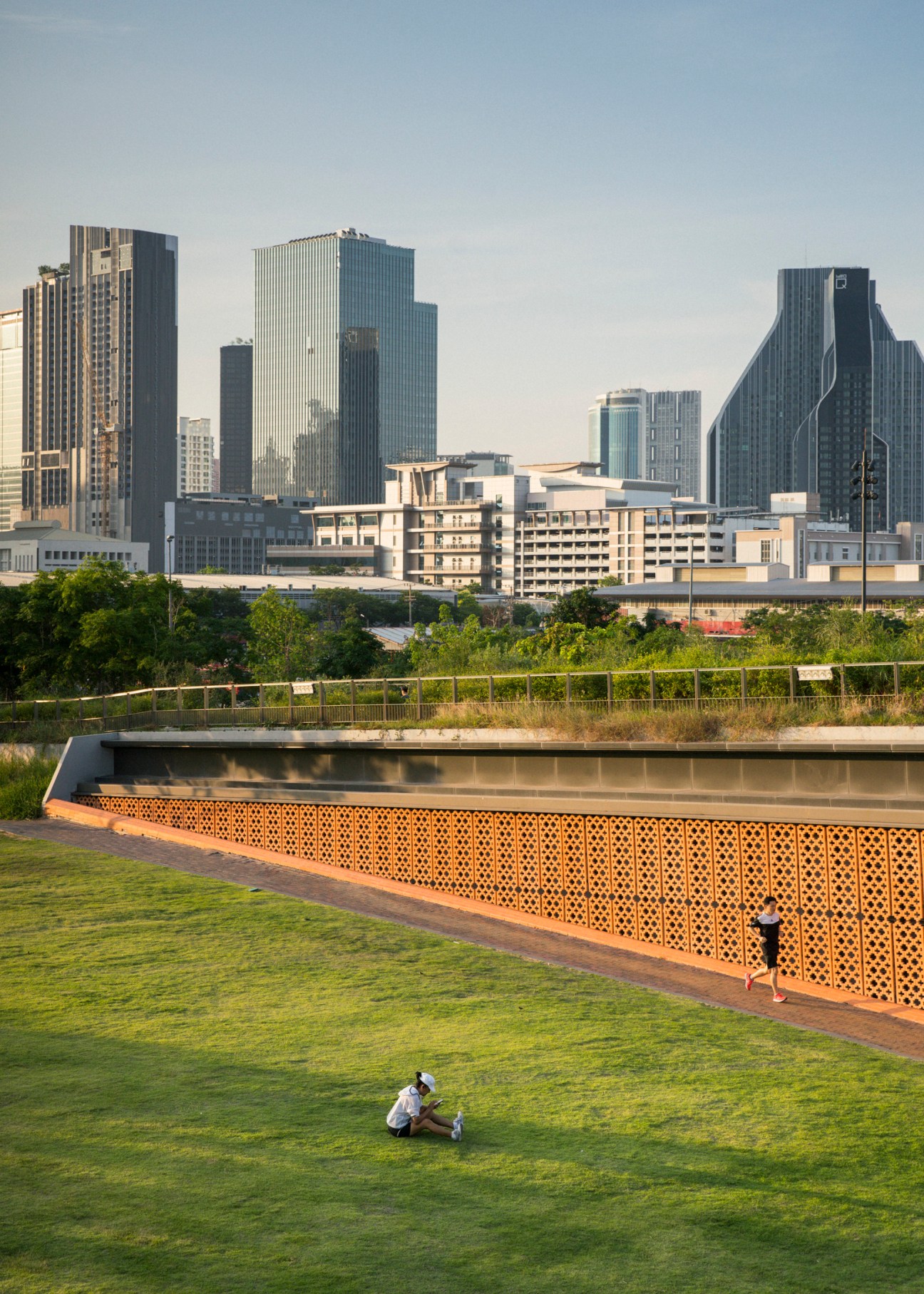 Person exercising on lawn at Centenary Park with Bangkok skyline and water feature behind.