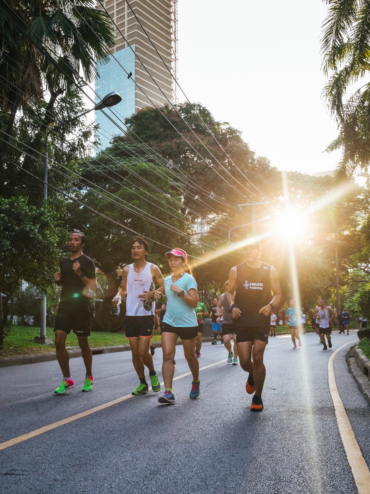 Group of joggers running on a tree-lined path at sunrise in Lumpini Park, Bangkok.