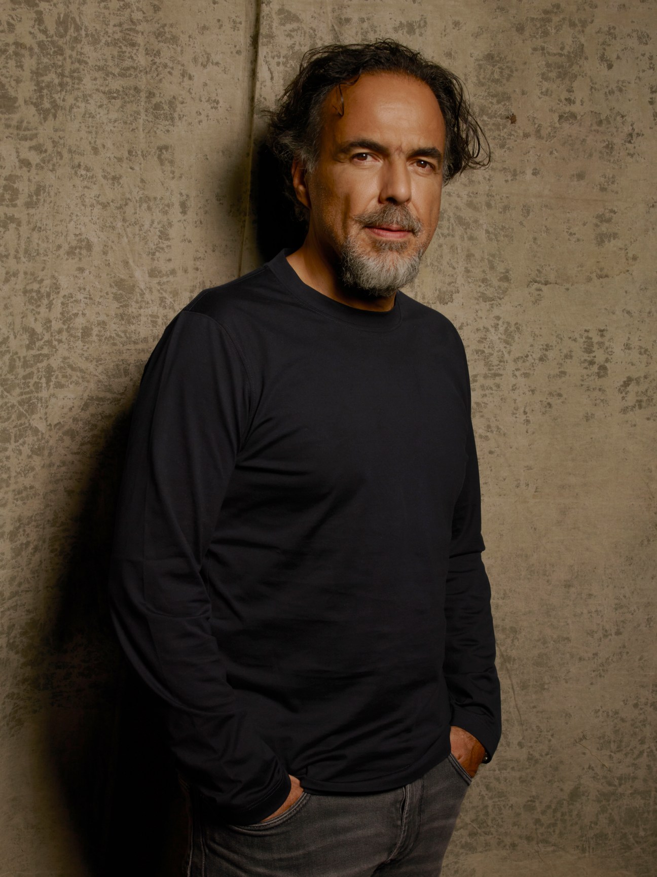 Alejandro González Iñárritu wearing a black long-sleeved shirt against a textured wall